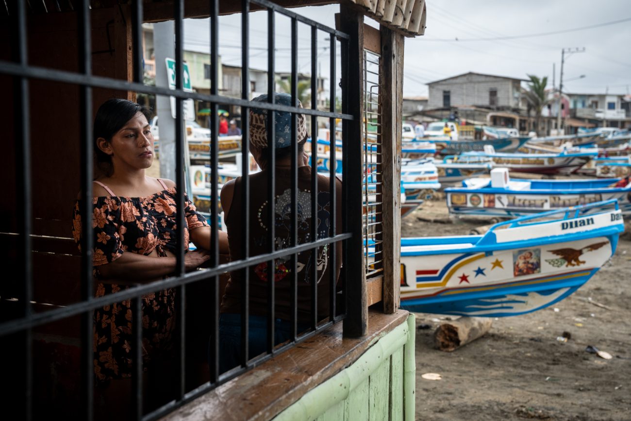 Taylor, una de las pocas enchaquirados que todavía salen a pescar, conversa con Vicky en la ventana del mercado que Vicky tiene en Puerto Engabao, donde vende comida, bebidas y productos de higiene para los pescadores artesanales. Foto: Irina Dambrauskas