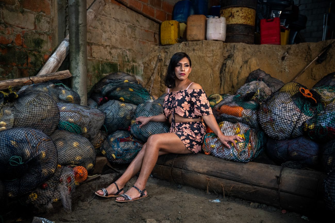 En la costa ecuatoriana, en la comuna ancestral de Engabao, aún resuenan los ecos de una historia que durante siglos fue silenciada: la de los enchaquirados, personas trans o de género no conforme que, en tiempos precolombinos, ocuparon un lugar sagrado dentro de la cultura huancavilca. Adornados con cuentas brillantes y conchas marinas —las chaquiras que les dieron nombre—, eran sacerdotes, guardianes de templos, figuras de respeto. Con la llegada del cristianismo y el avance del patriarcado, esa herencia fue arrinconada. Lo que alguna vez fue sagrado se volvió motivo de vergüenza o persecución. En tiempos modernos, la historia se transformó. Sin templos, sin altares, pero aún con fuerza, muchos enchaquirados encontraron en la pesca artesanal un nuevo espacio de existencia. En un oficio históricamente masculino, crearon una doble vida: por el día, faena y fuerza; por la noche, brillo, maquillaje y libertad. Pescar se convirtió en estrategia de supervivencia, pero también en acto de resistencia. Este proyecto retrata ese mundo. Mujeres como Vicky, Sarabia, Eliss, Rosalinda (hoy Oswaldo), y Taylor, la más joven de las que aún salen al mar, encarnan distintas formas de habitar esa herencia. Aunque muchas ya no pescan, ya sea por edad, enfermedades o por la violencia que hoy asola al sector pesquero, todas llevan en su historia una conexión con el mar. Un espacio que, como ellas, ha resistido. Hoy la pesca artesanal enfrenta una nueva crisis: piratería, crimen organizado, precariedad. Y con ella, desaparece también el espacio que durante años fue refugio para muchas personas trans en Ecuador. Los enchaquirados fueron, y aún son, parte esencial de la historia cultural del litoral ecuatoriano. En su resistencia cotidiana se entrelazan identidad, trabajo y territorio. Foto: Irina Dambrauskas