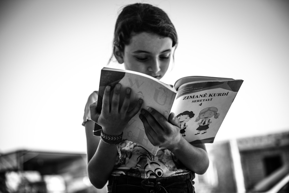 Kefa, niña de la comunidad koçer lee el cuaderno de aprendizaje de la lengua kurda brindado por la escuela pública de Rojava, 2023. Foto: Mauricio Centurion